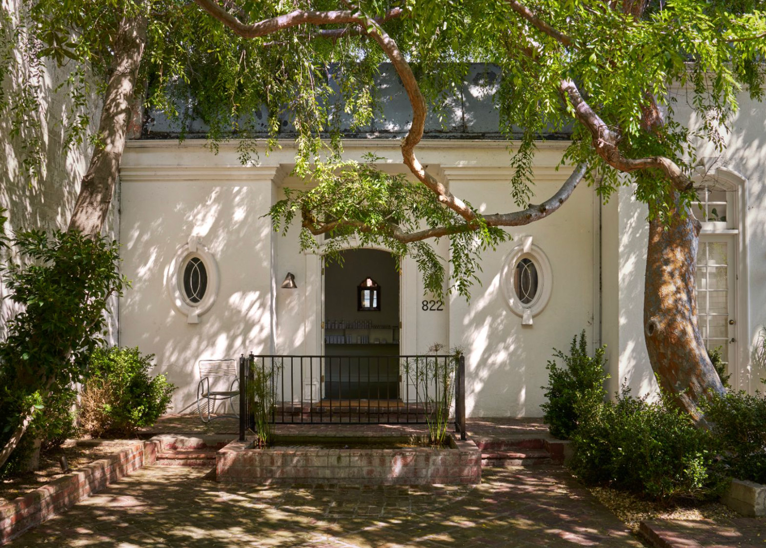 Entrance to Contrapposto at 822, white stucco facade with oval windows beneath a shade tree