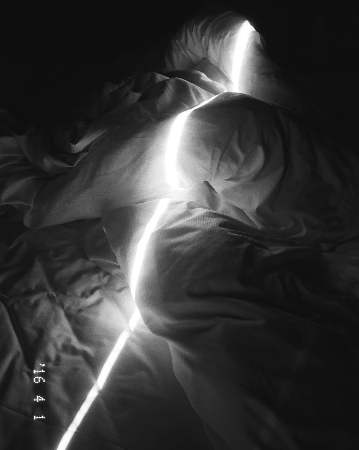 Figure wrapped in dark sheets with a line of bright light across the fabric, black and white