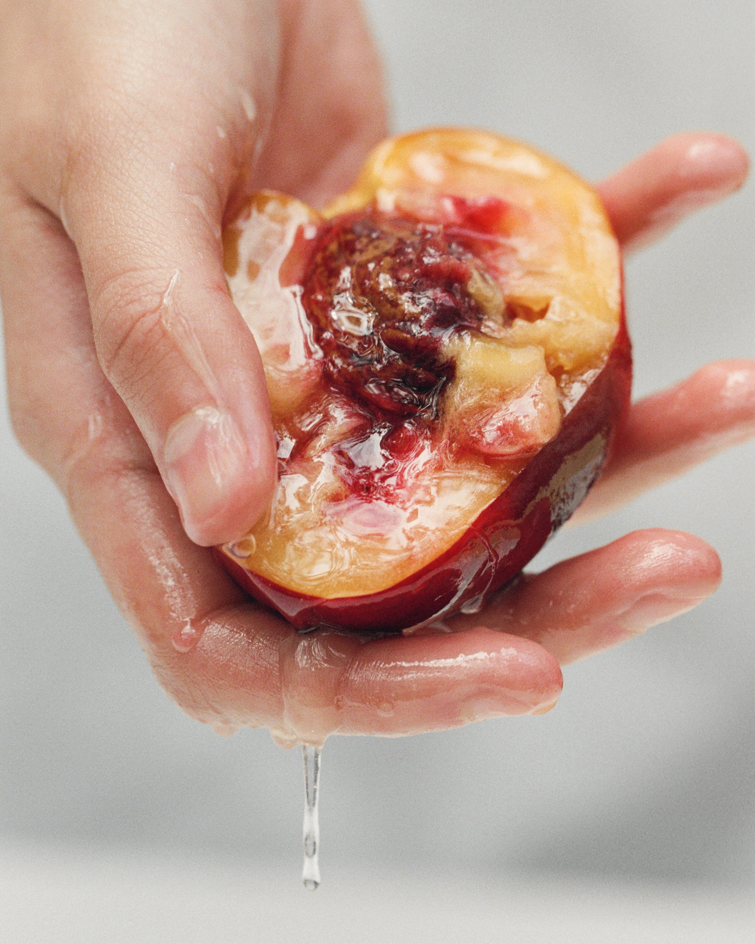 Hands squeezing a halved ripe peach, juice running between the fingers