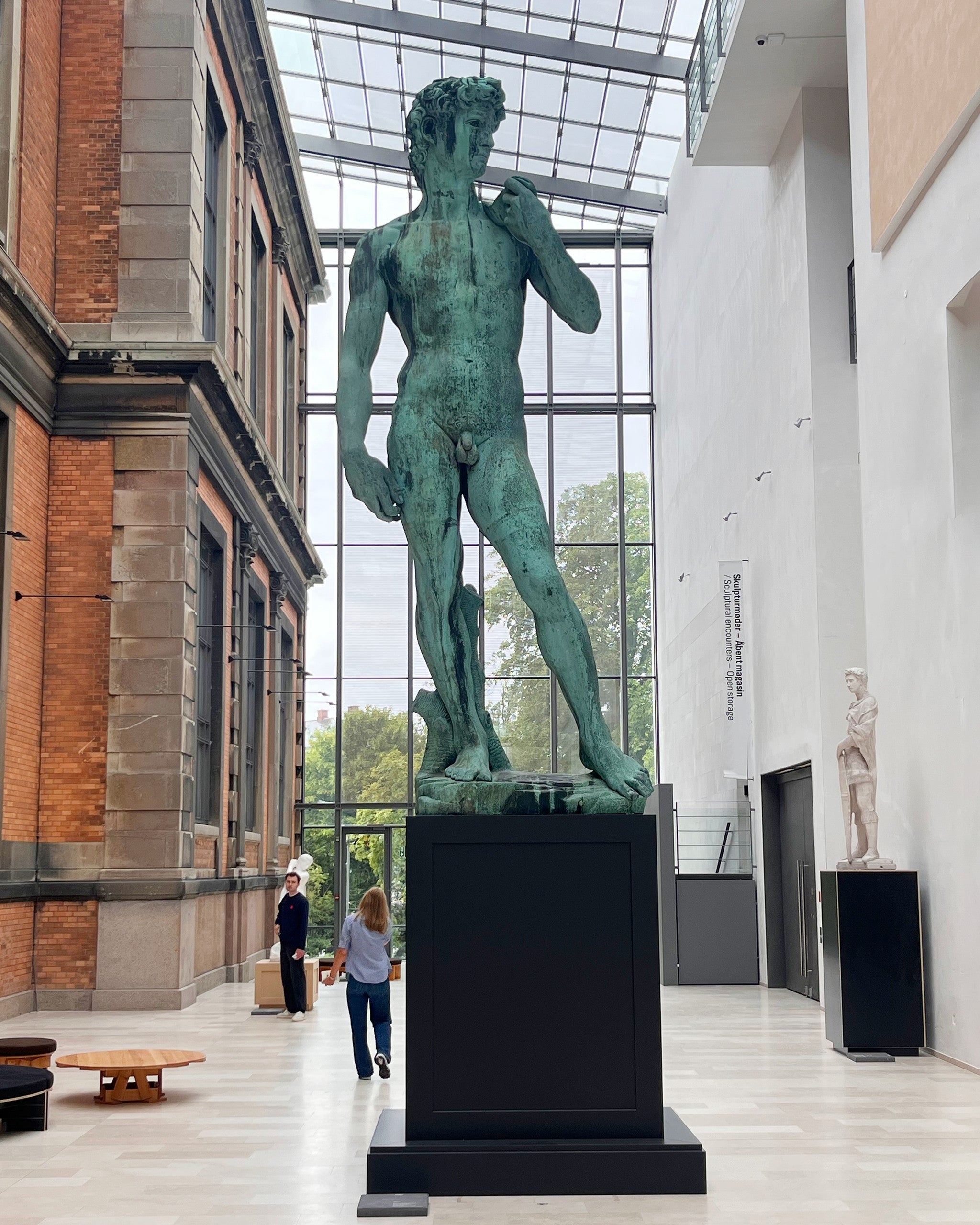 Bronze cast of Michelangelo's David on a black plinth in a glass-roofed museum hall